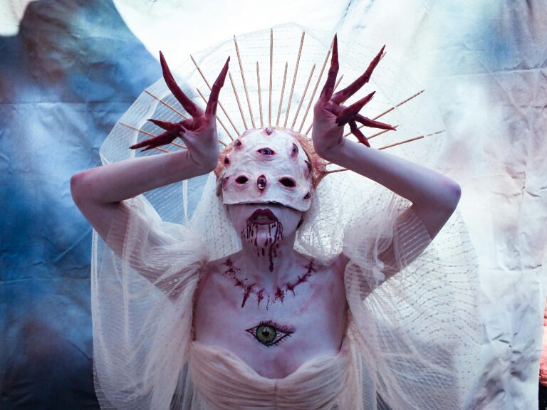 Surreal multi-eyed creature in white veil and crown with eerie makeup