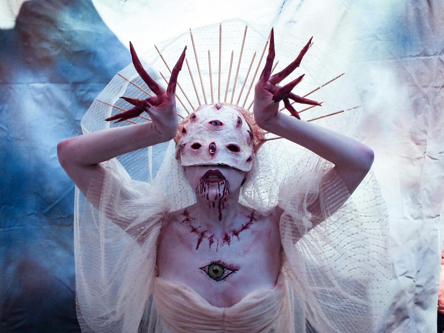 Surreal multi-eyed creature in white veil and crown with eerie makeup