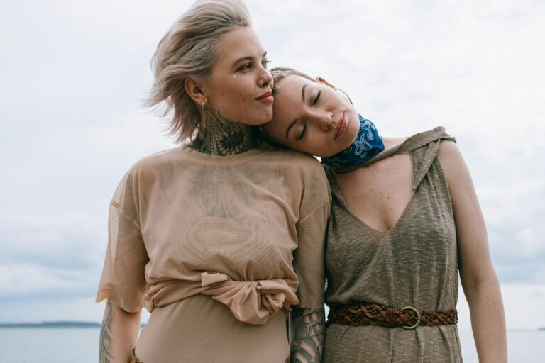 Two women sharing an intimate moment outdoors, one resting her head on the other's shoulder, symbolizing emotional and romantic connection.