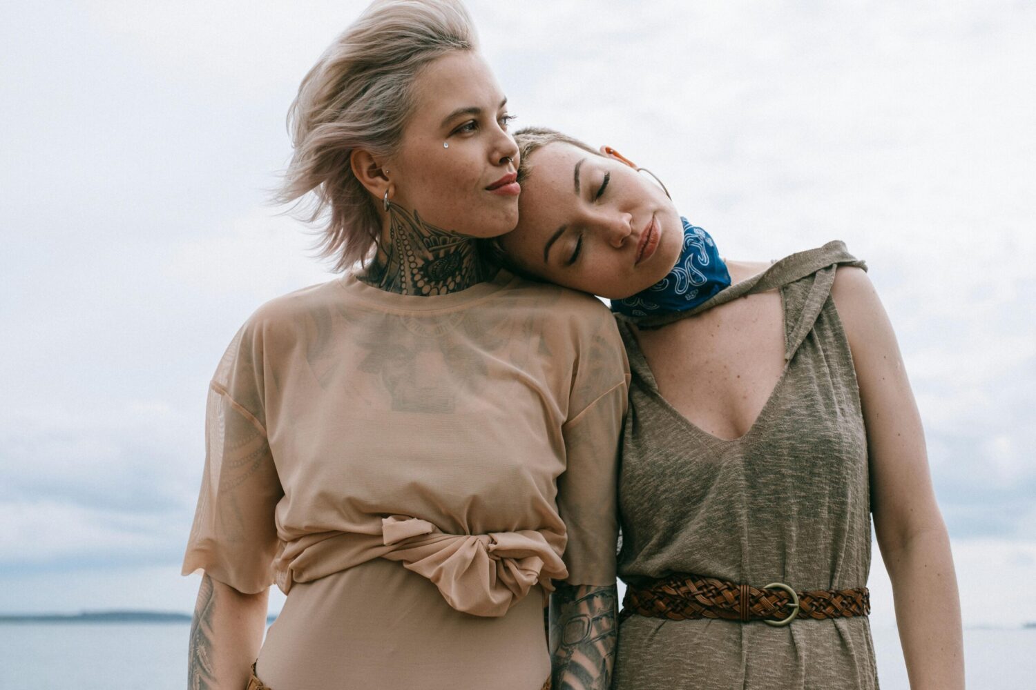 Two women sharing an intimate moment outdoors, one resting her head on the other's shoulder, symbolizing emotional and romantic connection.