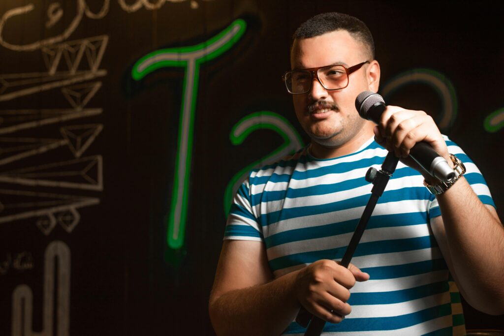 Comedian in striped shirt holding a microphone on stage during stand-up performance