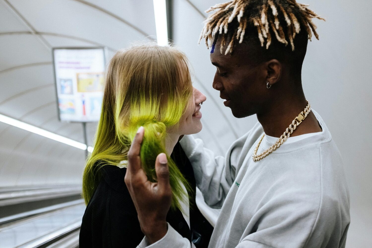 A young couple shares a playful, intimate moment on an escalator, smiling and gazing into each other's eyes.